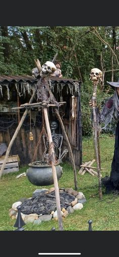 two people dressed up in halloween costumes and holding brooms, standing next to a wooden structure with skeletons on it