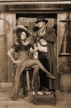 a man and woman dressed up in costume posing for a photo with an old fashioned western sign behind them