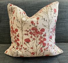 a white and red floral pillow sitting on top of a gray couch