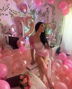 a woman sitting on top of a bed surrounded by pink and white balloons in the air