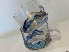 two glass mugs are stacked on top of each other with gold and blue designs