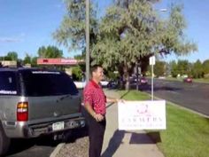 a man standing next to a sign on the side of a road in front of a car