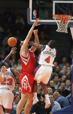 the basketball players are trying to block the ball from going into the hoop in front of the crowd