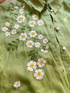 a green shirt with white daisies on the front and yellow centers in the back