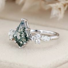 a green and white diamond ring with three diamonds on it's side, sitting on a pillow