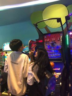 two people standing next to each other in front of pinball machines with neon lights