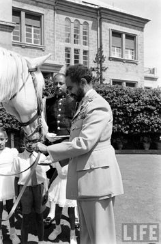 black and white photograph of man in uniform petting a horse