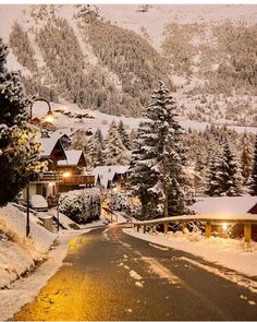 a snowy mountain with houses and trees in the foreground at night, lit up by street lights