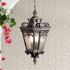 an old fashioned hanging light in front of a white brick wall with flowers on it