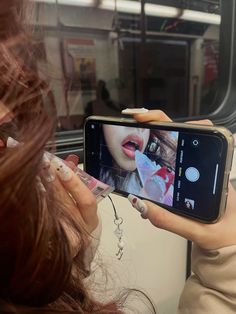 a woman taking a selfie with her cell phone on the subway train while she is brushing her teeth