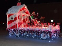 a christmas train decorated with lights and santa clause riding on it's back in the street