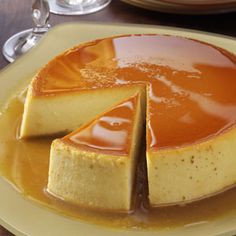 a cheesecake covered in caramel sauce on a yellow plate next to wine glasses