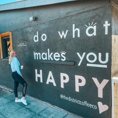 a woman standing in front of a building that says do what makes you happy