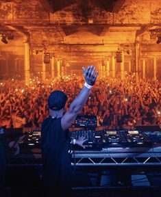 a dj in front of a large crowd with his hands up to the music on stage