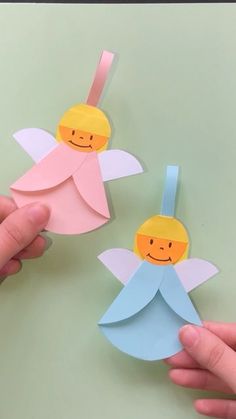 two handmade paper angel decorations on a green surface with one being held by the other