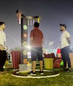 three men are standing in front of a sign with lights on it and trash cans