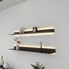 two floating shelves with lights on them in the corner of a white room next to a potted plant