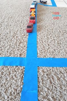 a toy train is on the ground next to a blue tape that looks like a cross