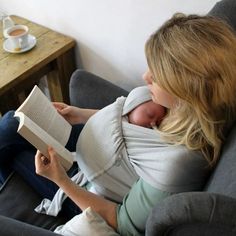 a woman is reading a book while sitting on a couch with a baby in her arms