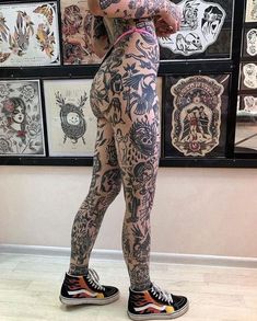 a woman with tattoos standing in front of a wall full of pictures and drawings on it