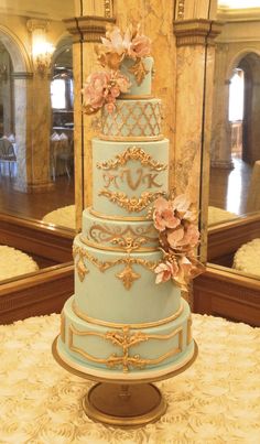 a blue and gold wedding cake with pink flowers on the top is sitting on a table