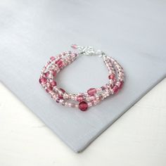 three strand bracelet with pink and white glass beads on a gray cloth place mat next to a silver chain