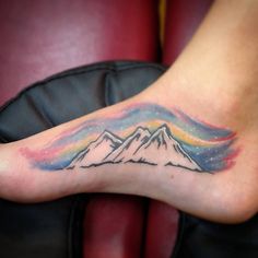 a tattoo on the foot of a person with mountains and rainbows in the background