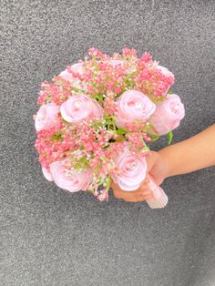 a person holding a bouquet of pink flowers in their hand on the ground with grey background