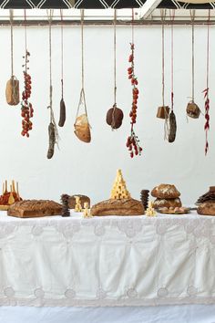 a table topped with lots of bread and pastries next to a wall hanging from the ceiling