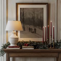 a christmas mantle with candles, books and pictures on it in front of a painting