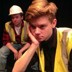 two young men sitting next to each other in front of a black background, one with his hand on his chin