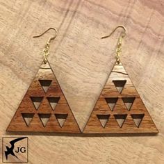 wooden earrings with triangles on them sitting on top of a piece of wood next to a pair of gold earwires