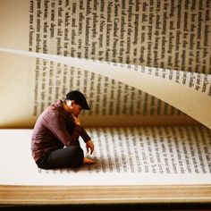 a man sitting on the floor in front of an open book with pages falling down