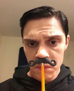 a man with a fake moustache on his face holding an orange pencil in front of his mouth