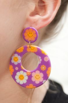 Step back in time and embrace the vibrant spirit of the 60s with our Purple Smiley Flower Power Chunky Hoop Earrings. These earrings are a fun and stylish accessory that pays homage to the iconic flower power era. Featuring a chunky hoop design adorned with cheerful flower smiley faces, these earrings exude retro charm. Crafted with super lightweight acrylic material, they are comfortable to wear while making a bold fashion statement. Product Details: Design: Our Purple Smiley Flower Power Chunk Flower Smiley, Smiley Flower, 60s Jewelry, Purple Accessories, Chunky Hoop Earrings, Hoop Design, Smiley Faces, 70s Inspired, Step Back