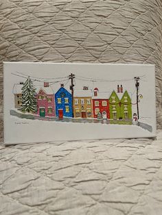 a card with houses painted on it sitting on a bed