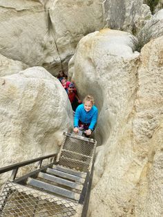 a woman climbing up the side of a mountain on a metal stair case in between two large rocks