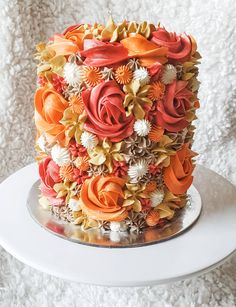 a multi - colored cake with flowers on top sits on a white plate and is ready to be eaten