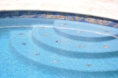 an empty swimming pool with blue water and rocks on the edge is pictured in this image