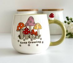 two coffee mugs sitting next to each other on a white table with mushrooms painted on them