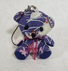 a small purple teddy bear with pink flowers on it's head and eyes is hanging from a key chain