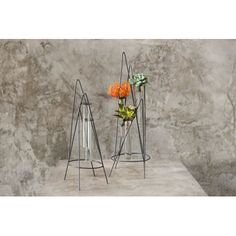 two metal vases with flowers in them on a shelf next to a stone wall