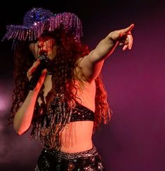 a woman with long red hair wearing a purple hat and holding a microphone in her hand