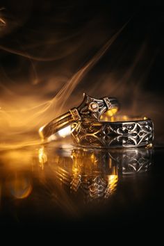 two gold wedding rings sitting next to each other on top of a reflective surface in the dark