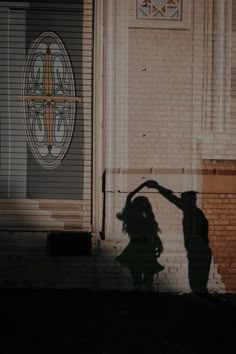 the shadow of two people in front of a building with a cross painted on it