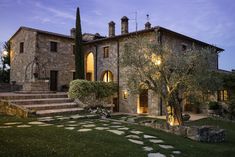 a stone house with steps leading up to it and trees in the front yard at night