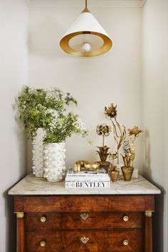 a wooden dresser topped with vases filled with flowers and greenery next to a lamp