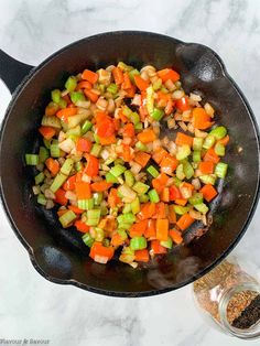 a skillet filled with chopped vegetables on top of a white counter next to seasoning