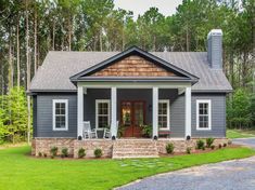 a small gray house with white trim and two porches on the front, surrounded by trees