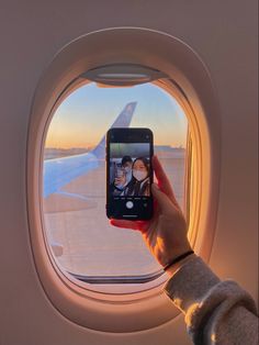 a person holding up a cell phone in front of an airplane window